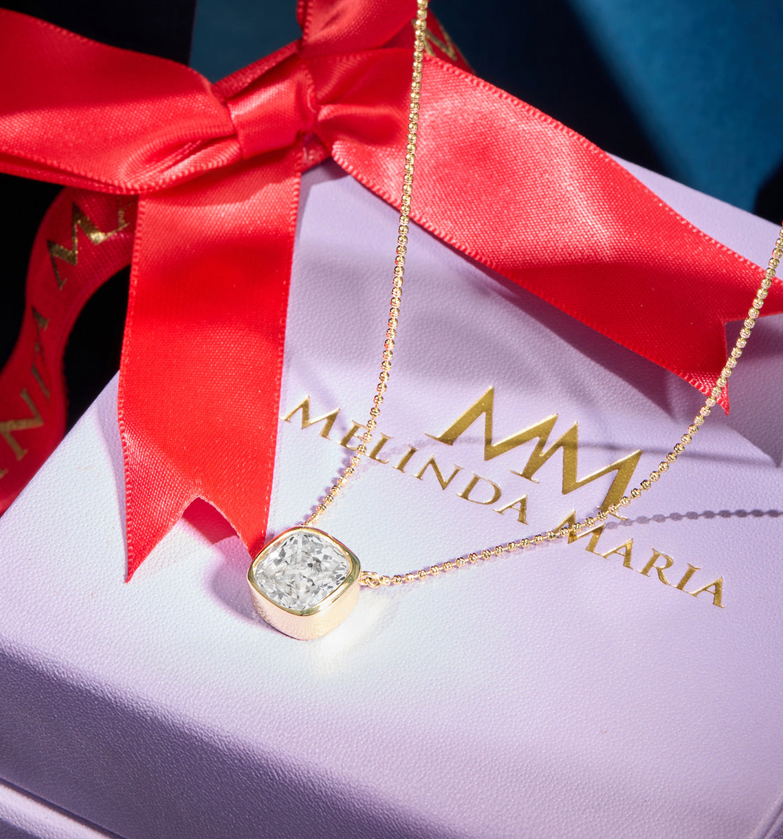 Gold necklace with a diamond pendant on a Melinda Maria box with a red ribbon.