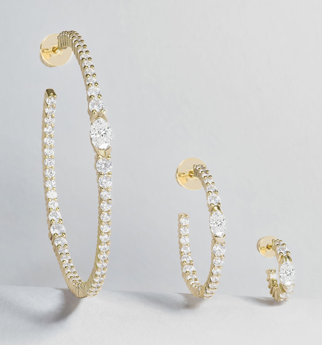 Gold hoop earrings with clear gemstones on a light gray background