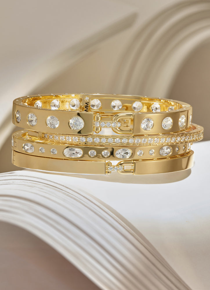 Gold bracelets with clear stones on a textured beige surface