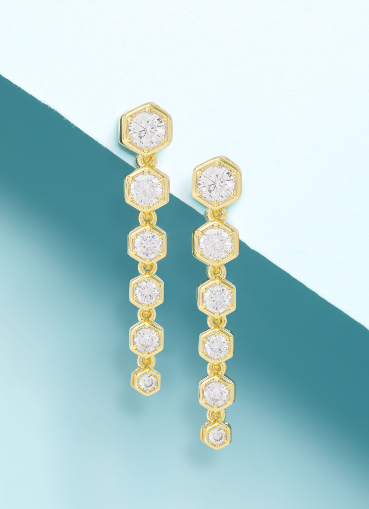 Gold earrings with clear gemstones on a gradient blue background