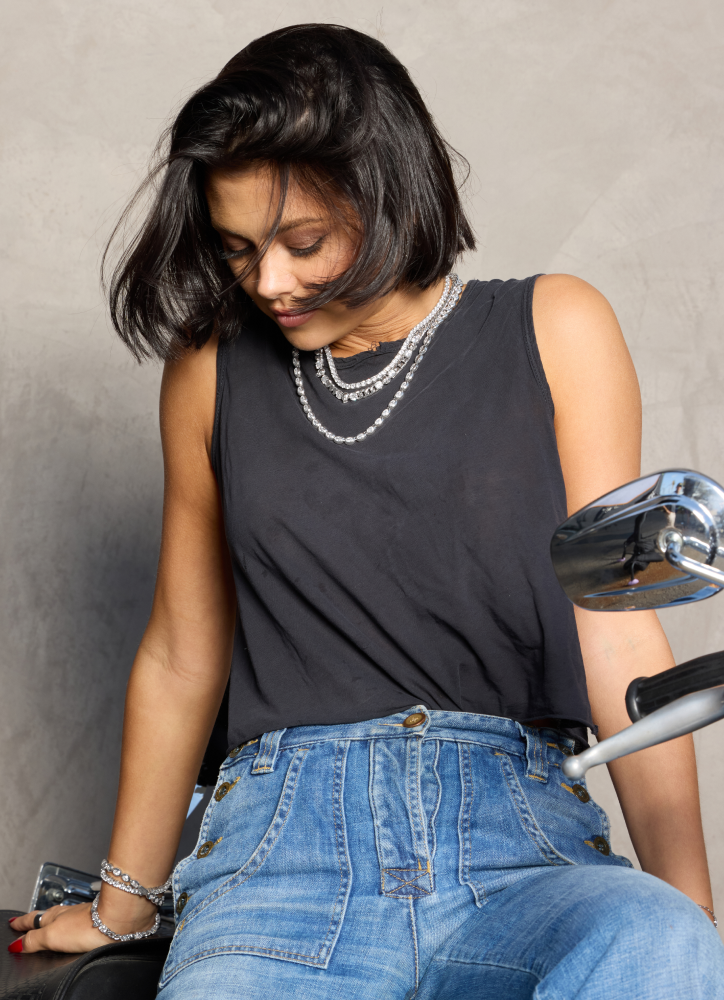 Woman sitting on a chair wearing a black sleeveless top and blue jeans, with a neutral background.