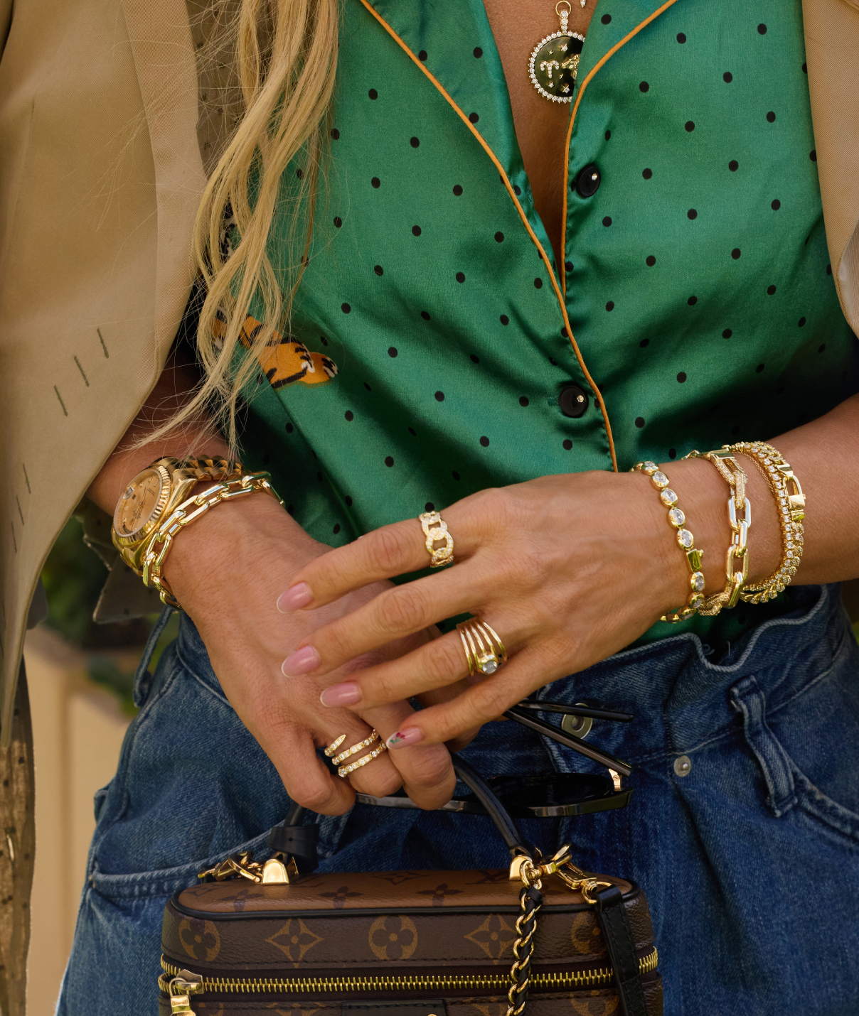 Close-up of a person wearing gold jewelry with a green polka dot shirt and blue jeans.