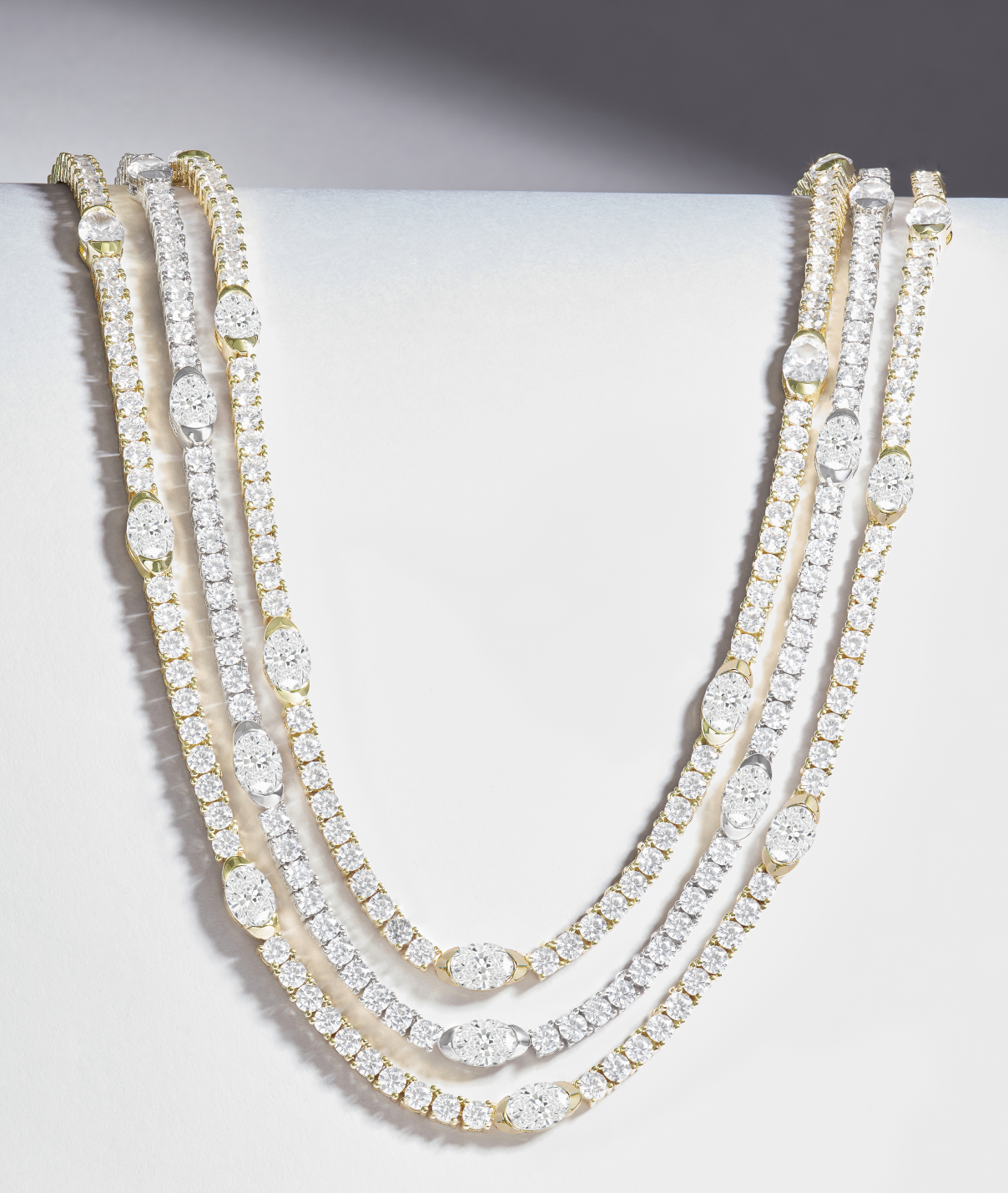Three diamond necklaces on a light gray surface
