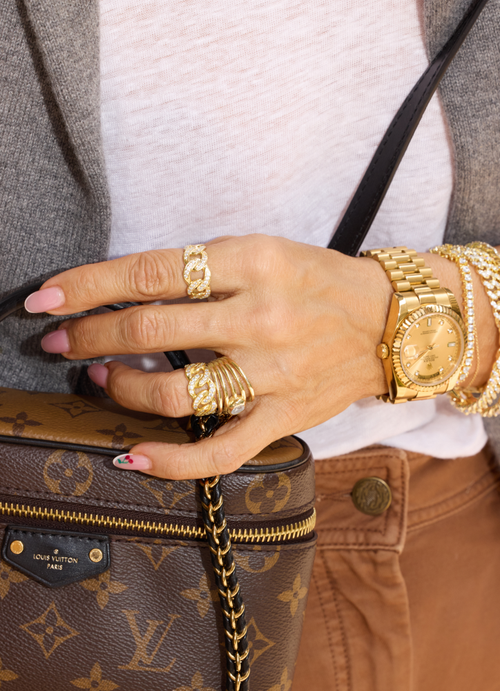 Hand with gold rings and bracelets holding a Louis Vuitton handbag.