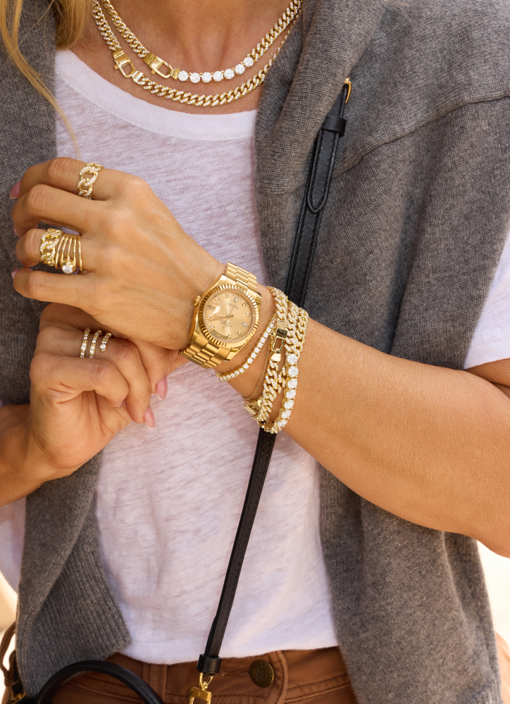 Close-up of a person wearing gold jewelry including a watch, bracelets, and rings.