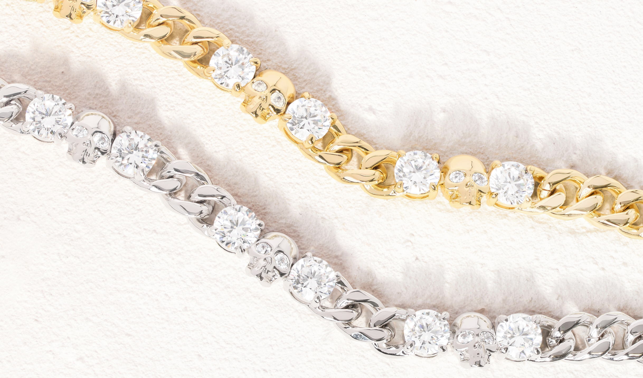 Two diamond-encrusted bracelets, one gold and one silver, on a light background.