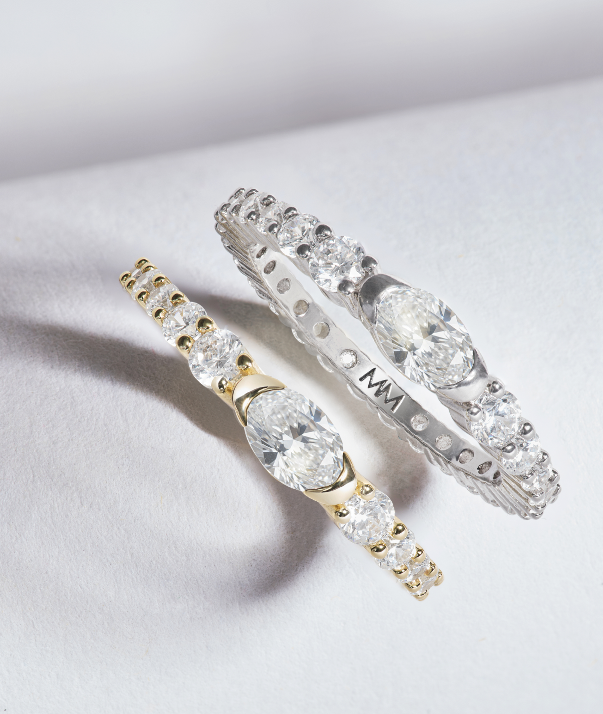 Two diamond rings, one gold and one silver, on a light gray background