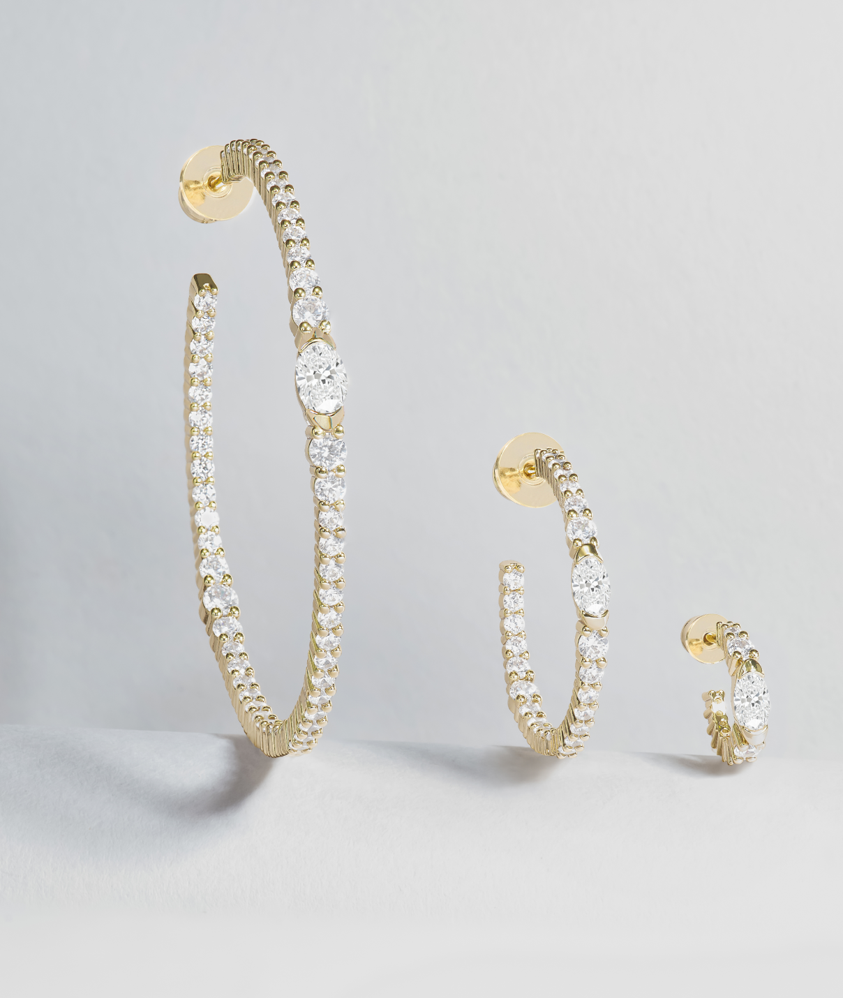 Gold hoop earrings with clear gemstones on a light gray background