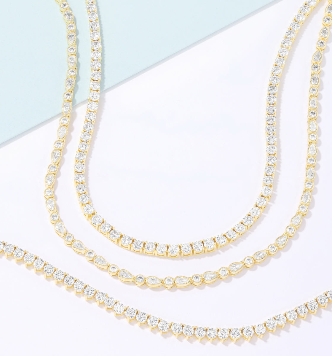 Two gold necklaces with clear gemstones on a light blue and white background