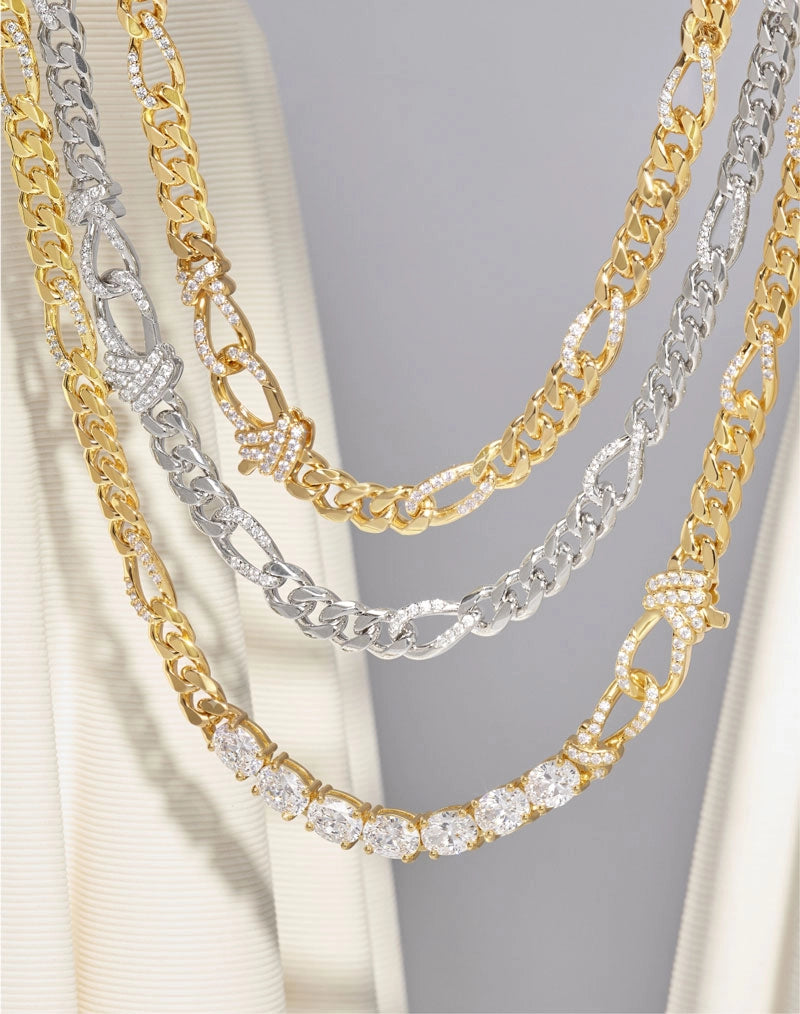 Three layered gold and silver-tone chains with clear rhinestone and crystal embellishments, displayed on a cream-colored garment against a light gray background.