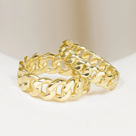 A gold-toned chunky curb-link chain ring, photographed on a clean, light beige studio background.