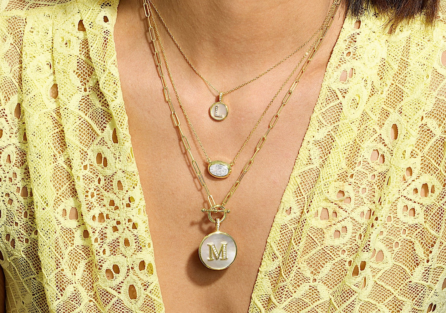 Necklace with a 'M' pendant worn under a yellow lace garment