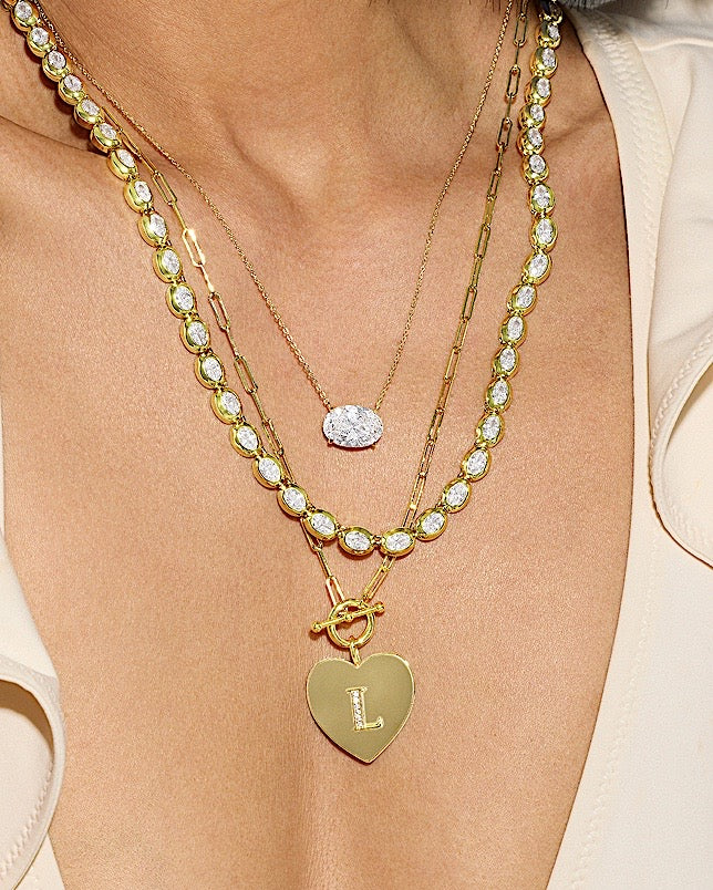 Gold necklaces with heart-shaped pendant and clear gemstones on a beige background