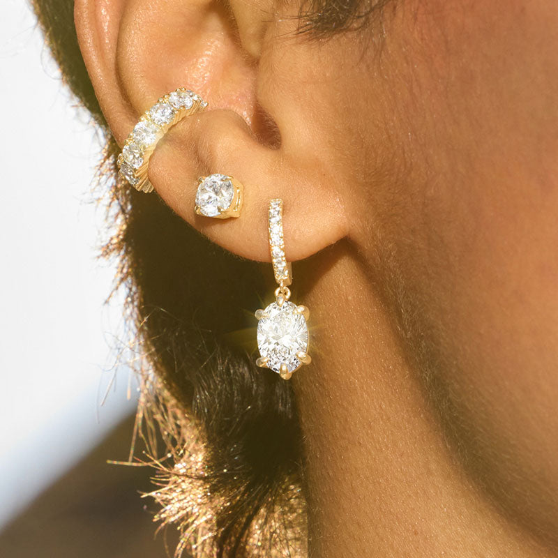 Close-up of a person wearing gold hoop earrings and a diamond earring.