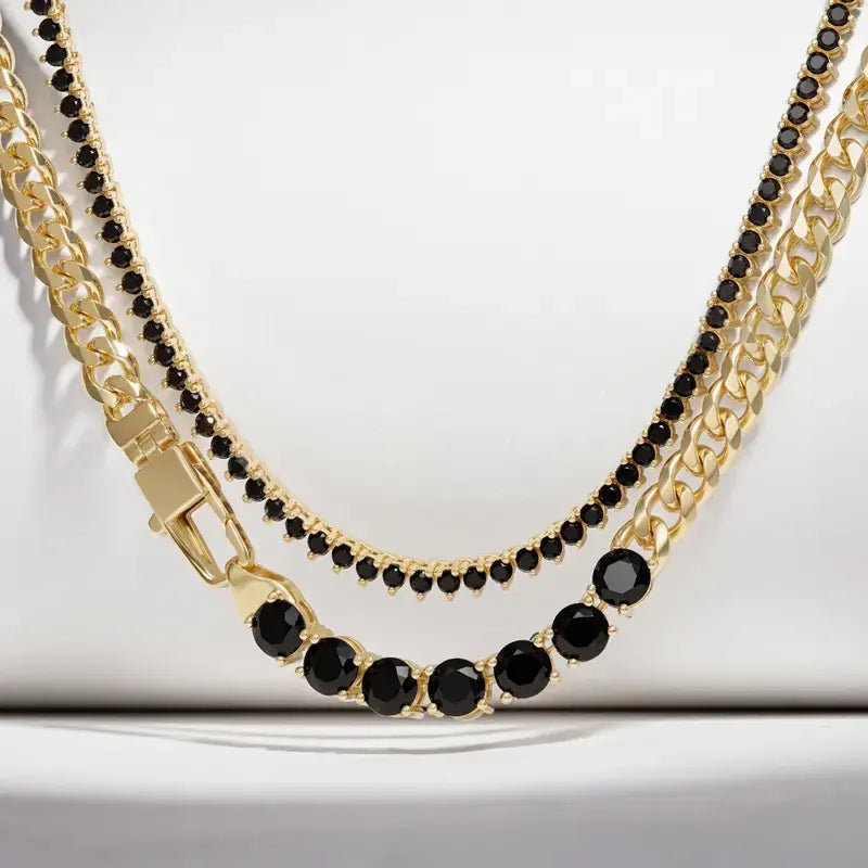 Gold-tone chain necklace with black faceted gemstones, featuring a curb chain, a fine bead chain, and a tennis-style link section with round black stones, displayed on a white background.