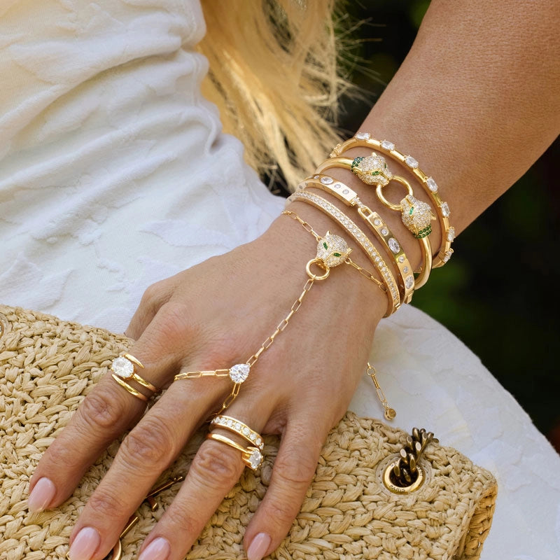 Model wearing a stack of gold bracelets with a raffia handbag