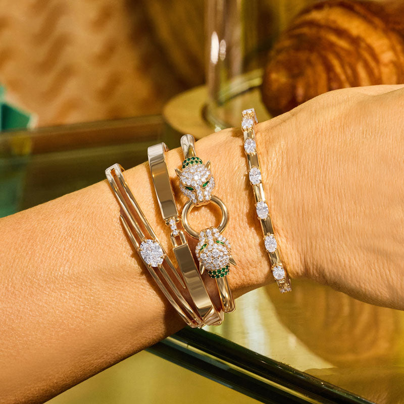 Close-up of a wrist wearing multiple gold and diamond bracelets with a blurred background
