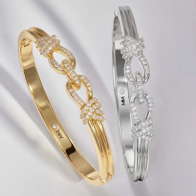 Two bangle bracelets displayed on a light gray background, one in yellow gold and one in silver. Both feature a polished band with three interlocking knot-like links paved with small clear stones.