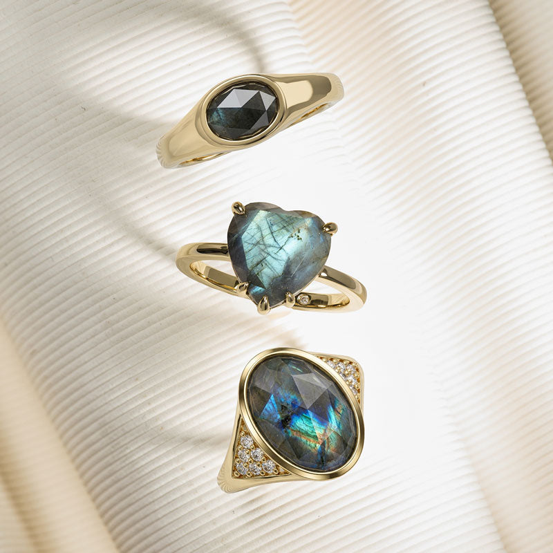 Three gold rings with labradorite stones on a textured beige background
