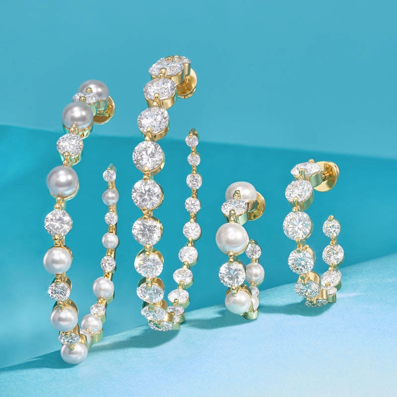 Gold-tone jewelry set featuring pearl and diamond drop earrings and matching chain necklaces, arranged on a smooth light blue surface.