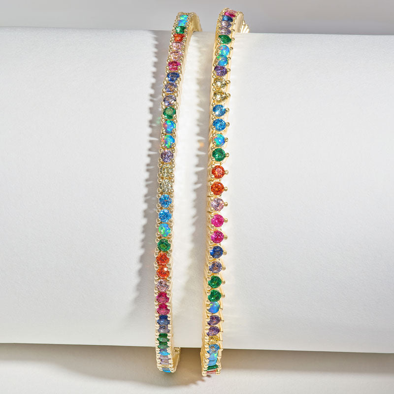 Gold hoop earrings with multicolored gemstones on a white surface