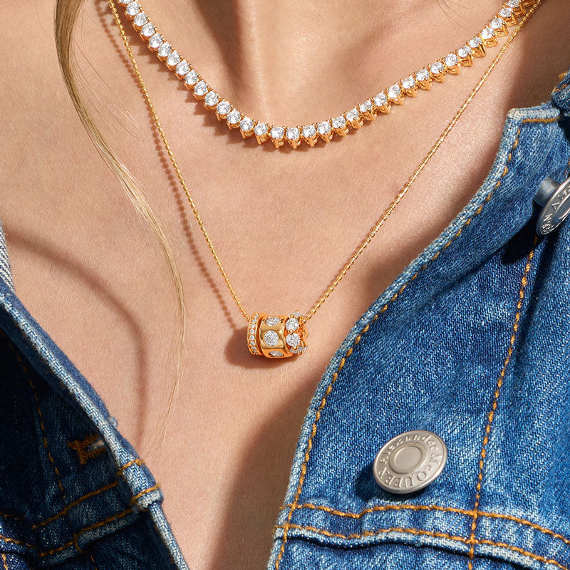 Close-up of a person wearing two gold necklaces with diamond pendants, one on a denim jacket.