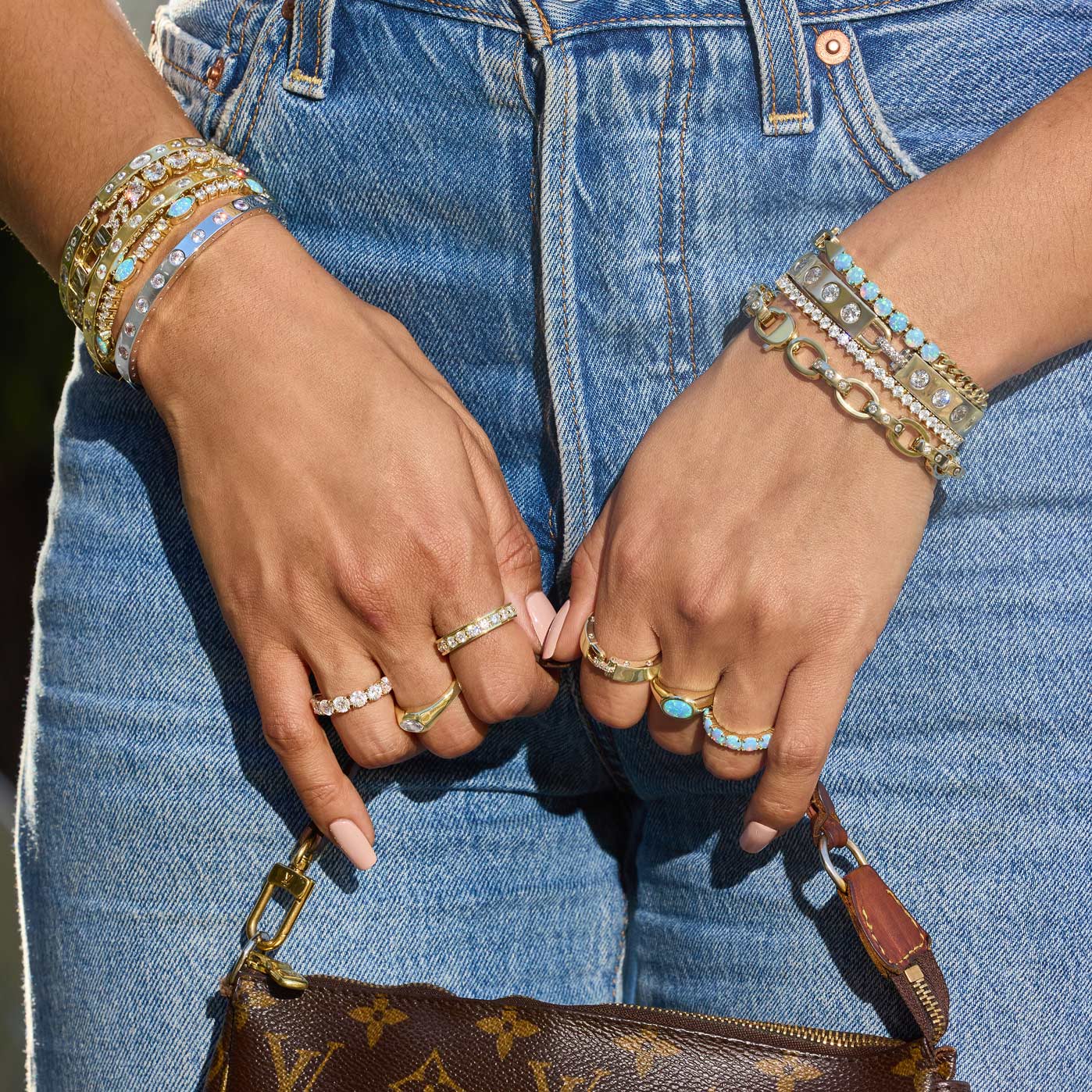 Close-up of hands with jewelry holding a brown handbag, wearing blue jeans.
