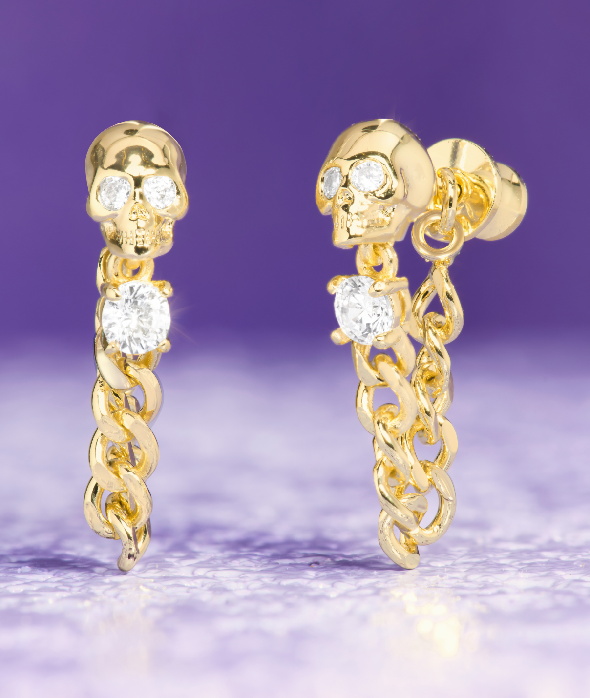 Gold skull earrings with chain details on a purple background
