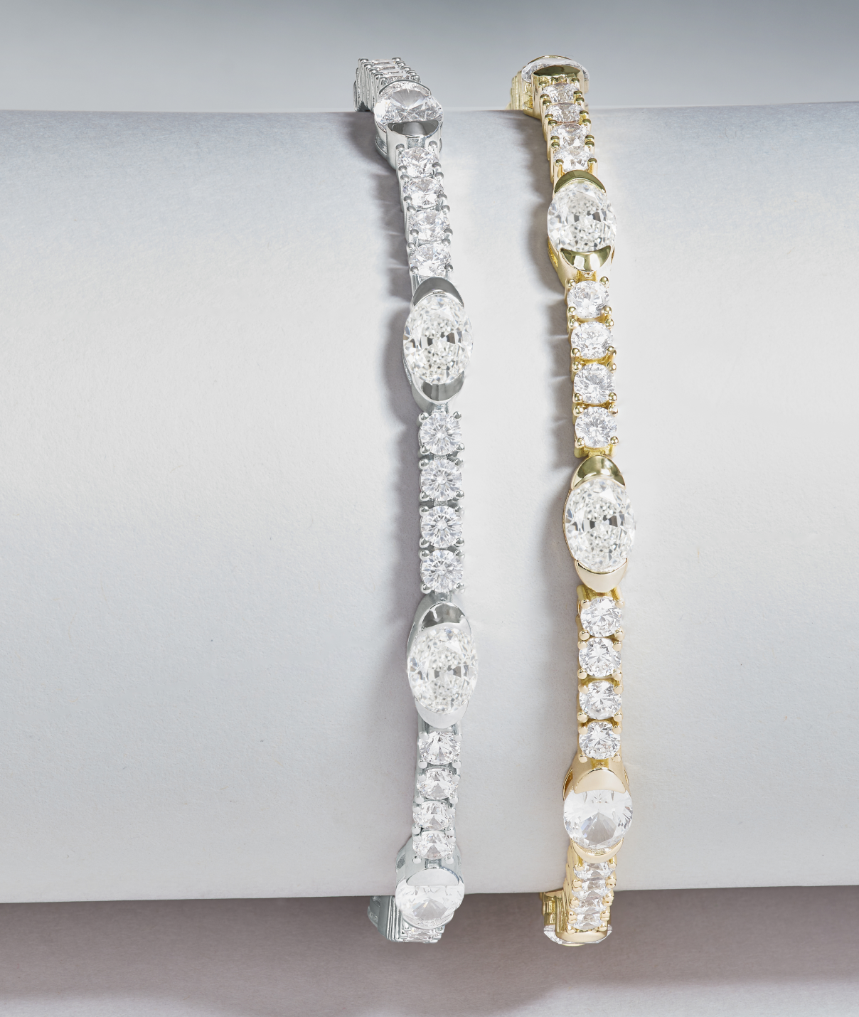 Two diamond bracelets, one gold and one silver, on a light gray background