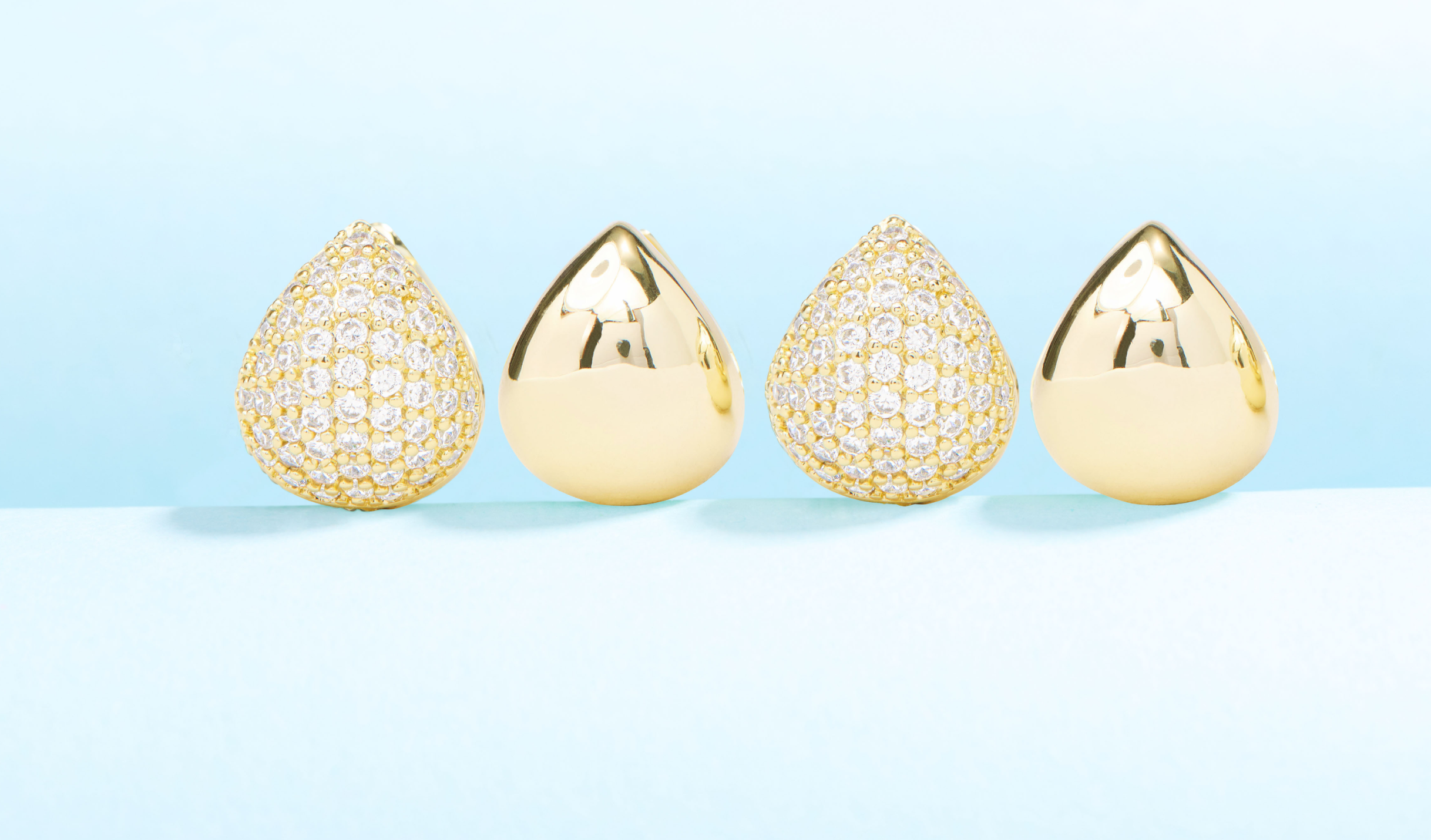 Pair of gold teardrop-shaped earrings with diamond accents on a light blue background