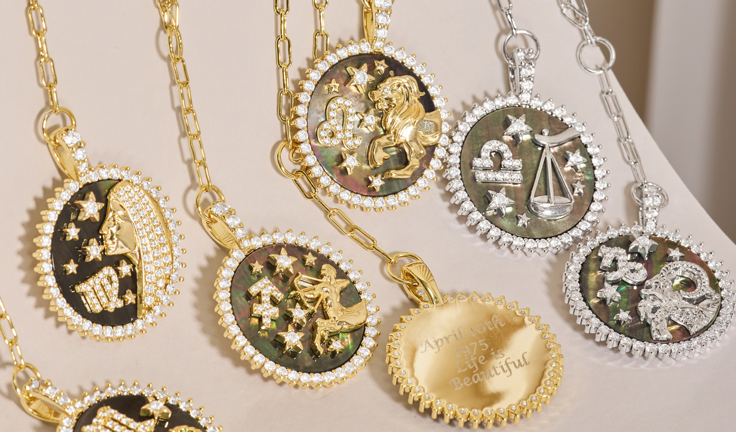 Collection of gold and silver necklaces with zodiac pendants on a neutral background