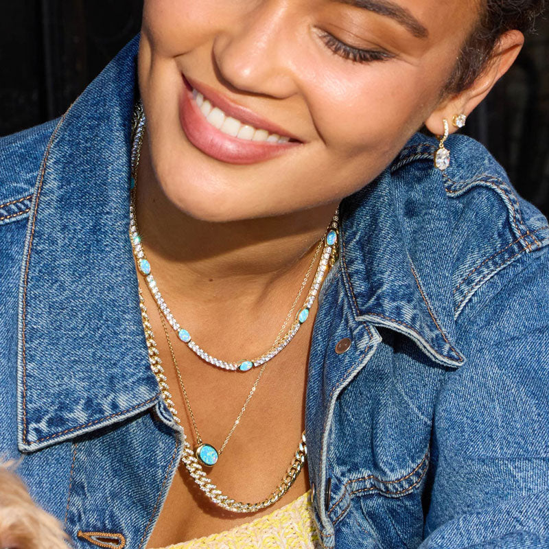 Woman wearing a denim jacket with layered necklaces and earrings.